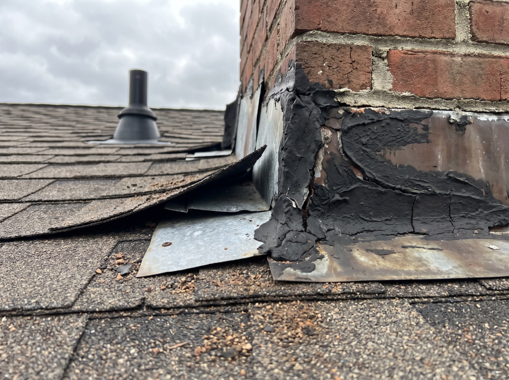 A brick chimney on an asphalt shingle roof with failed roof-cement flashing and a lifted shingle, marked up with numbered pins, a circle and an arrow