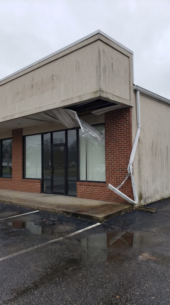 A storefront with torn soffit panels and a bent downspout, marked up with numbered pins, a box and an arrow